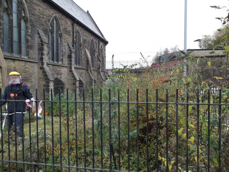 A volunteer with a strimmer clears away overgrowth on the church's corner plot
